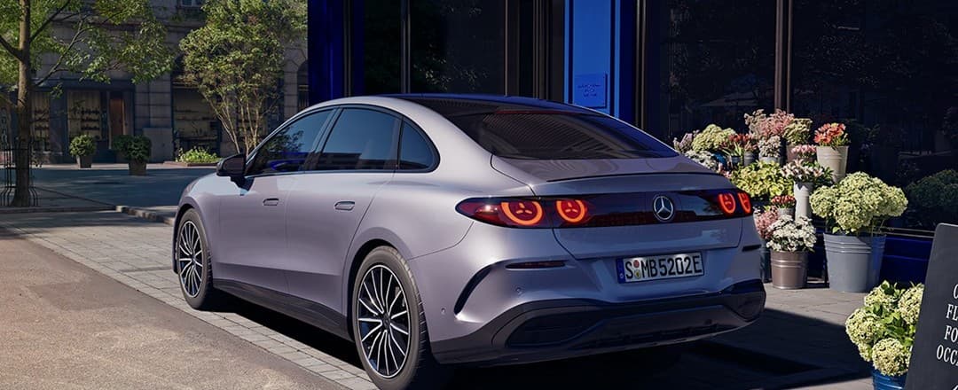 Nuevo Mercedes-Benz Clase C eléctrico plateado visto desde atrás, aparcado ante una floristería de fachada azul