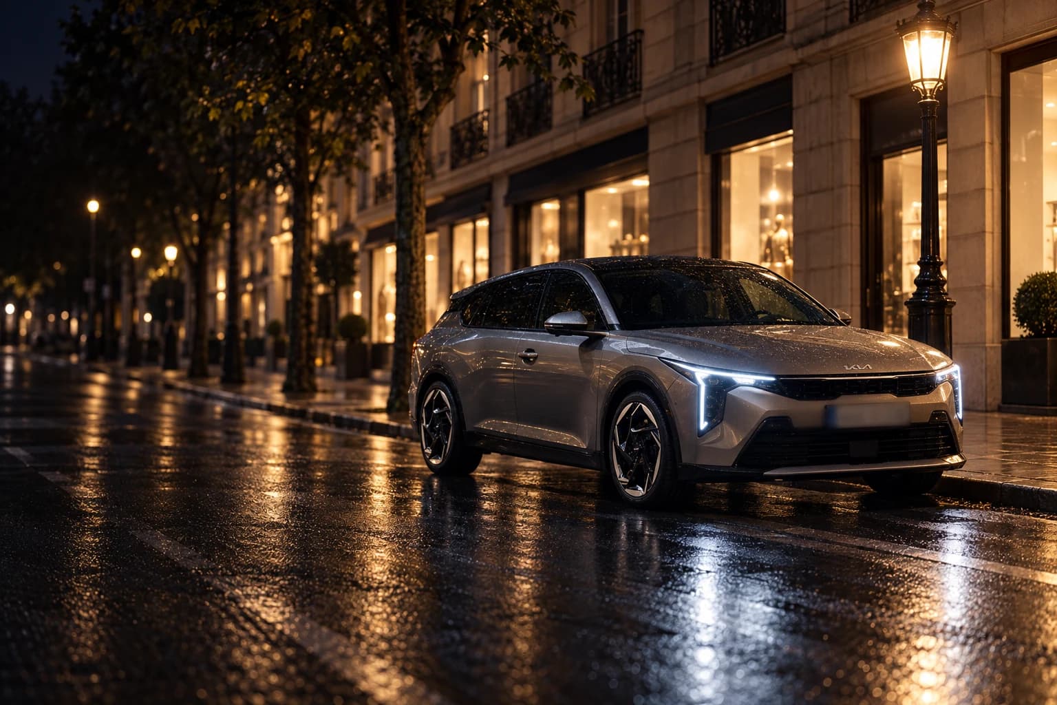Kia K4 gris aparcado de noche en una calle de Madrid, con los faros encendidos reflejados en el asfalto mojado