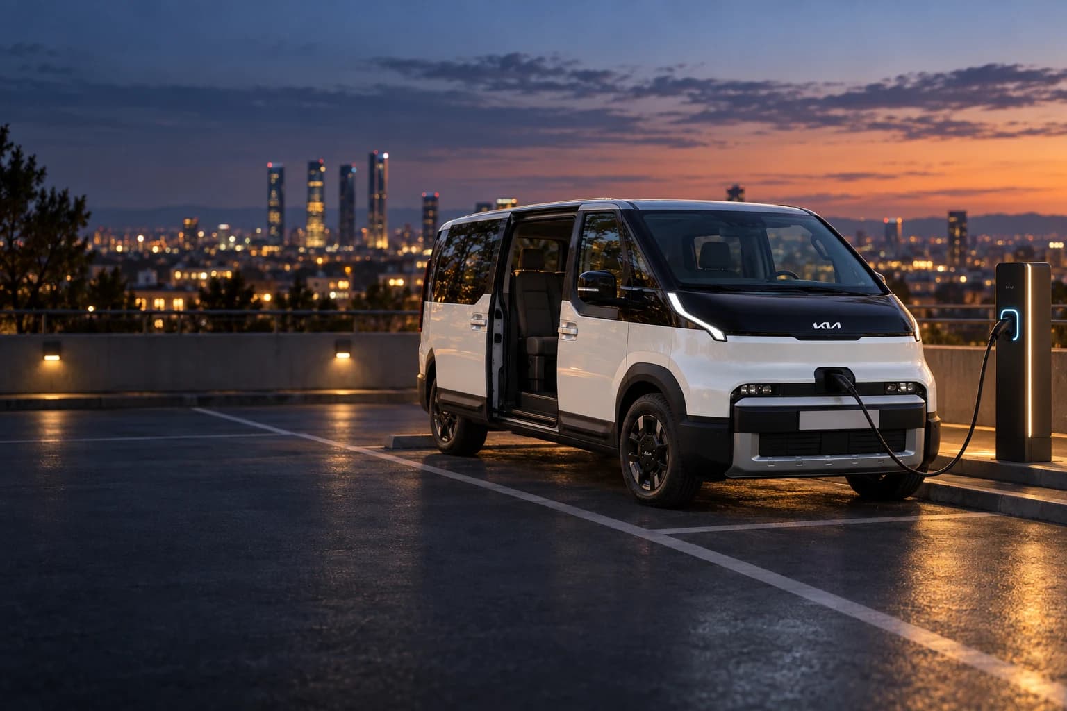 Kia PV5 Passenger enchufada a un punto de recarga al anochecer, con Madrid iluminada al fondo