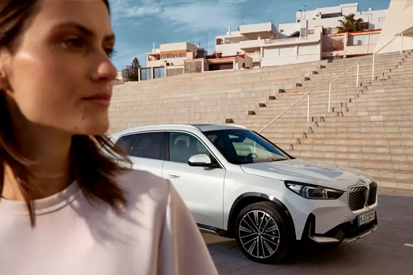 BMW iX1 mujer en exterior Mujer posicionada delante del BMW iX1 blanco aparcado en la calle